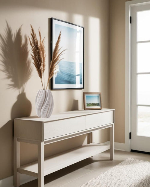 3D printed white ceramic vase with pampas grass on light wood console table, styled in a coastal entryway with ocean artwork and neutral beige walls.