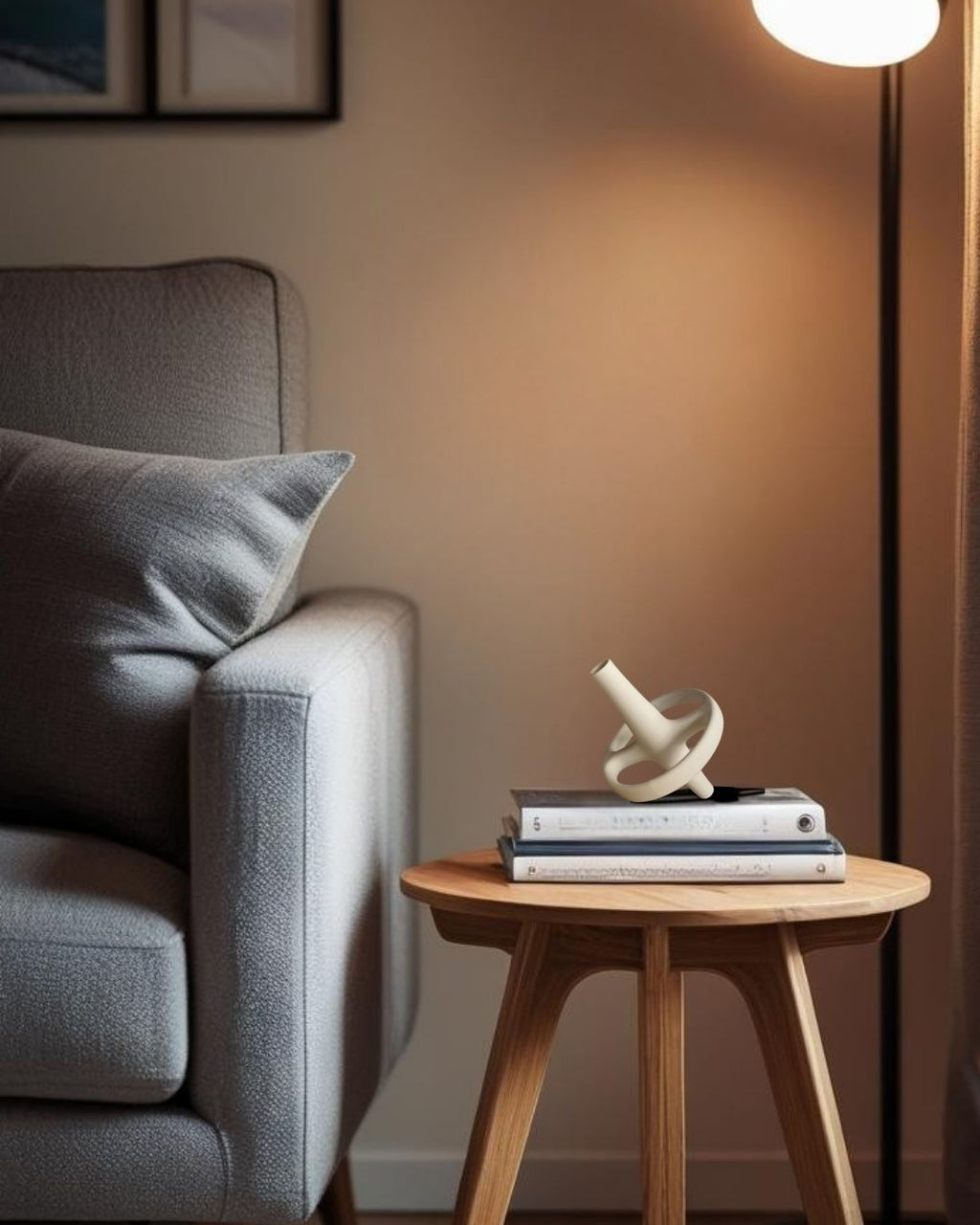 Gray sofa with a wooden end table holding books and a decorative accent, against a neutral wall.