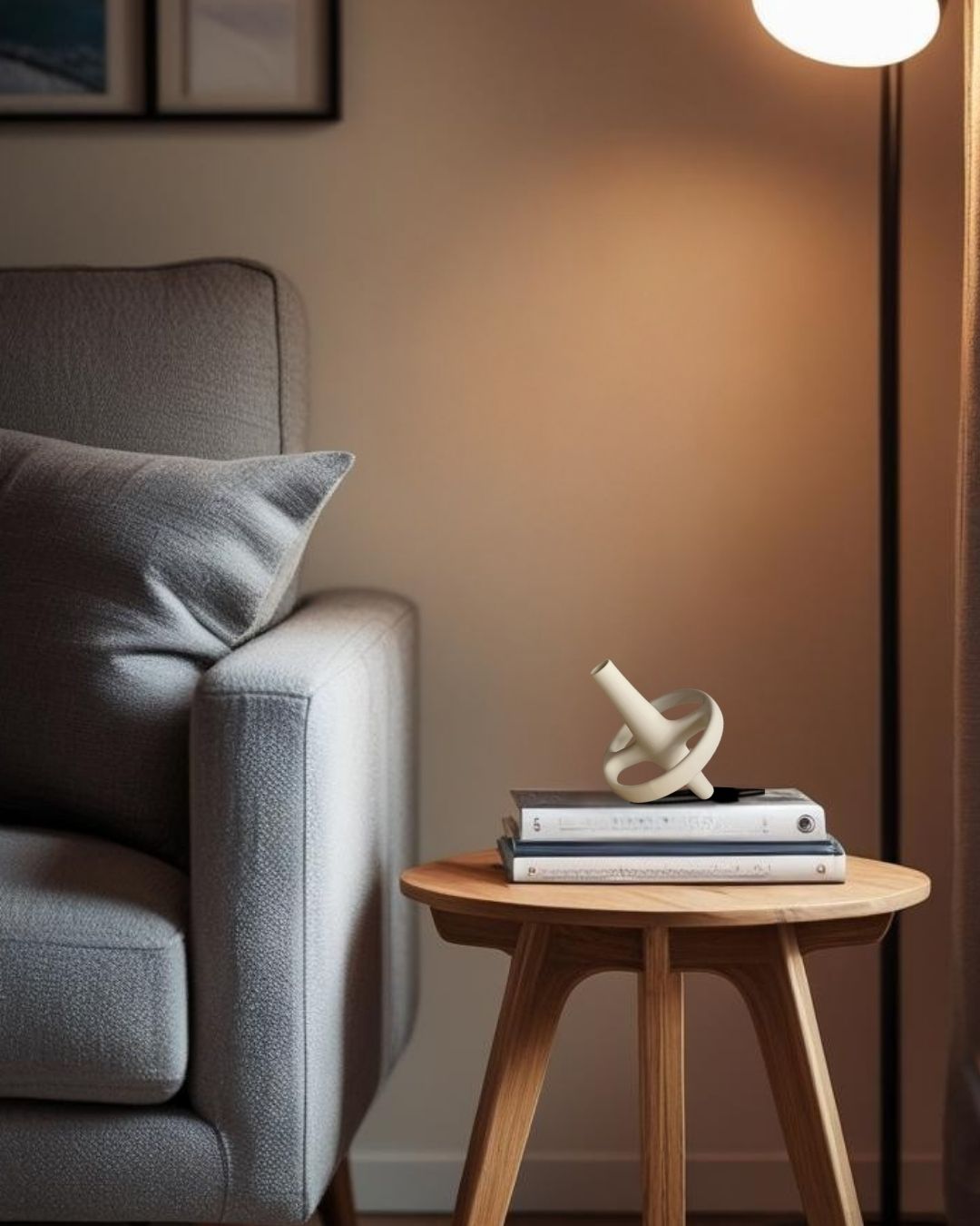 Gray sofa with a wooden end table holding books and a decorative accent, against a neutral wall.