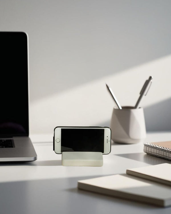 White minimalist smartphone stand on modern desk with laptop, pen holder, and natural light