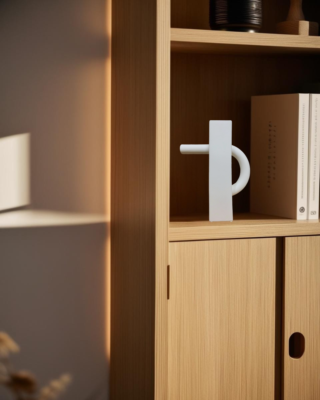 Abstract white geometric decorative pitcher on natural wood bookcase shelf with modern books and soft sunlight in a minimalist interior
