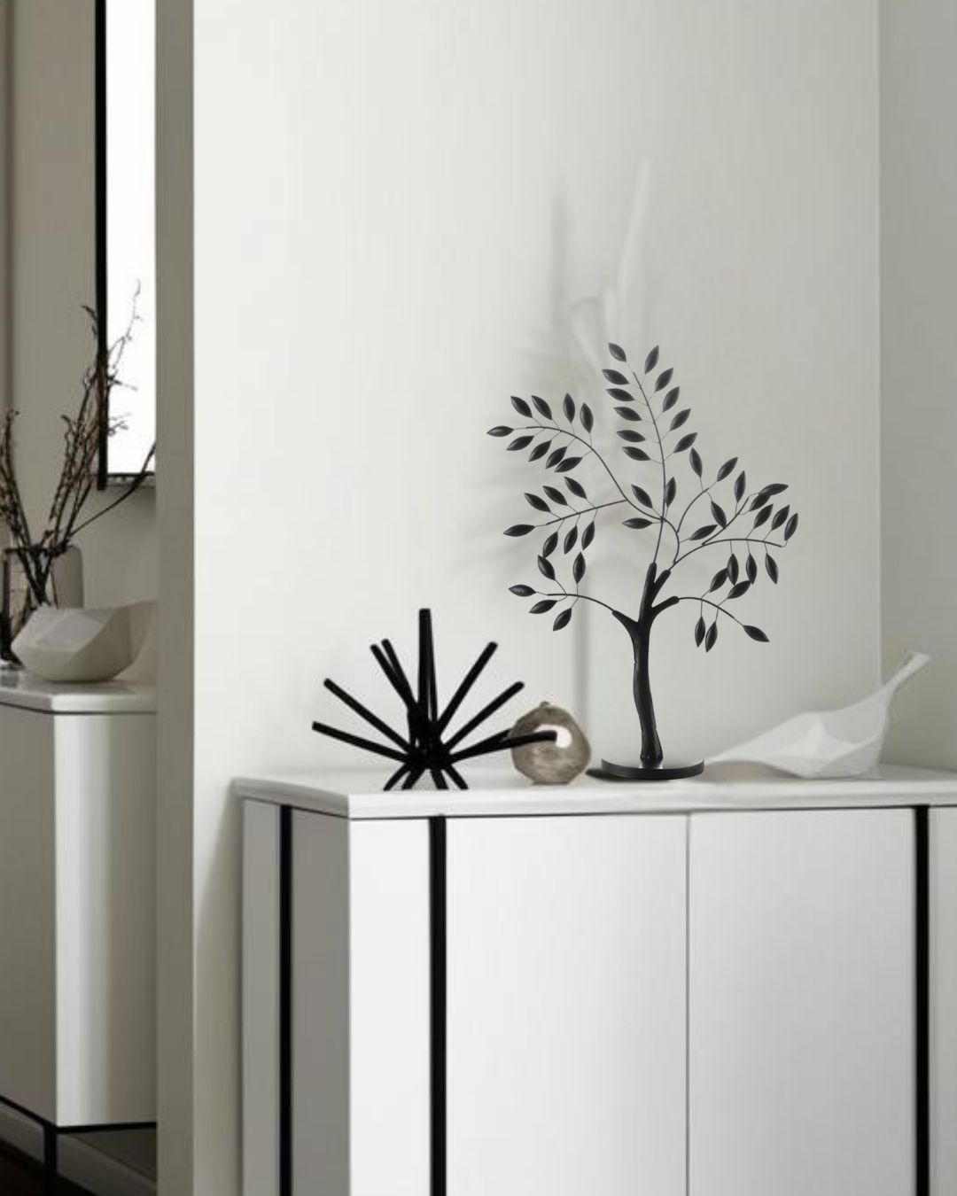 Black metal nature-inspired decorative accent tree on modern white sideboard with minimalist sculptures in a contemporary interior setting