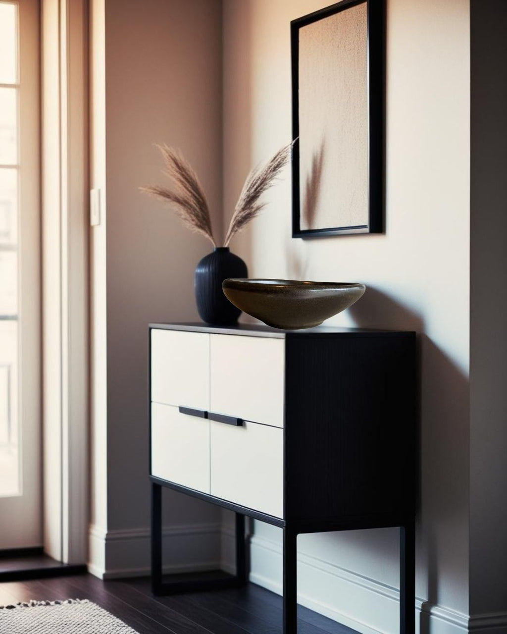 Black sculptural porcelain decorative bowl on a two-tone console in a Scandinavian style entryway with framed art and natural light