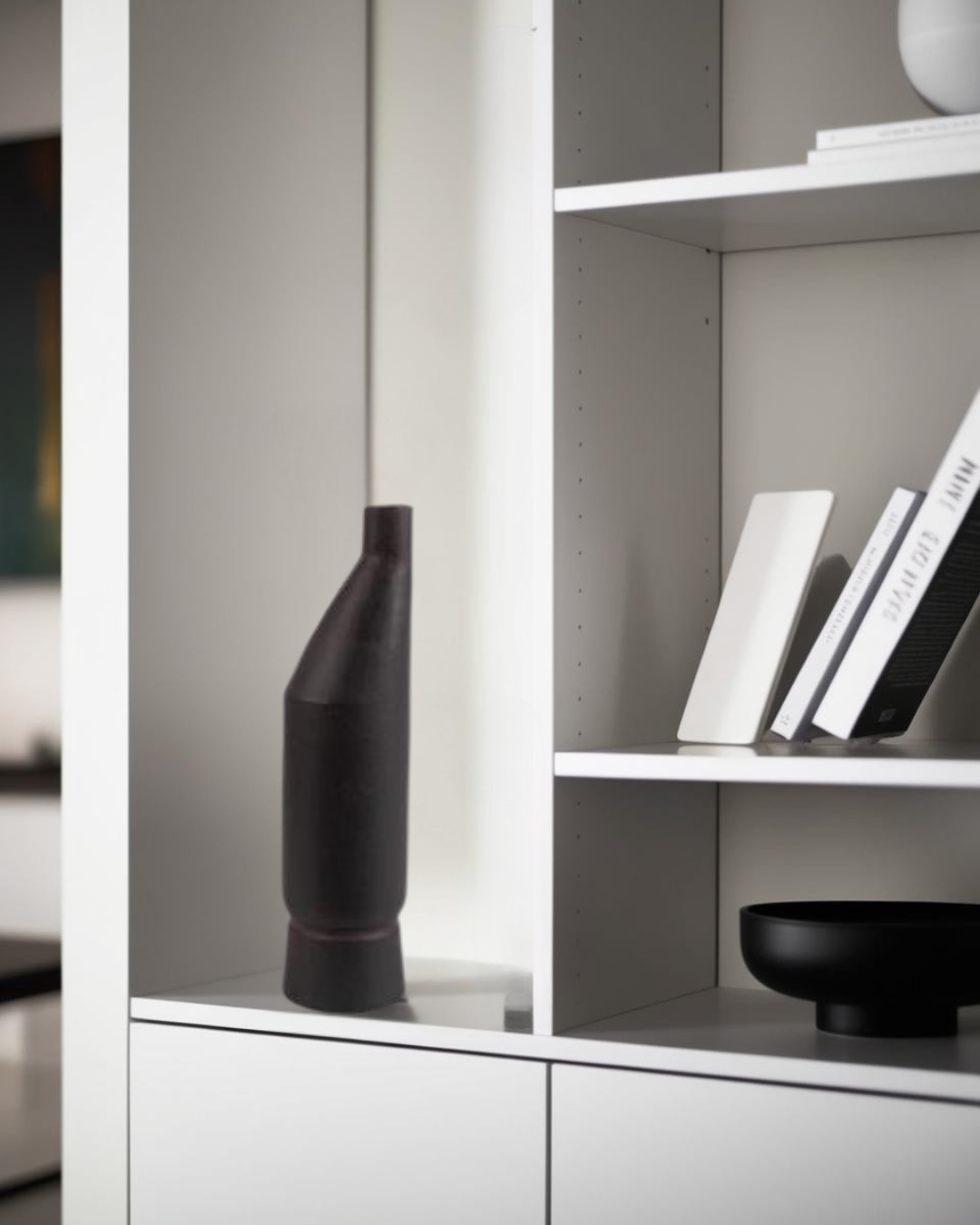 Tall black ceramic vase displayed on a white shelf, styled with minimalist decor and monochrome books in a modern living space.







