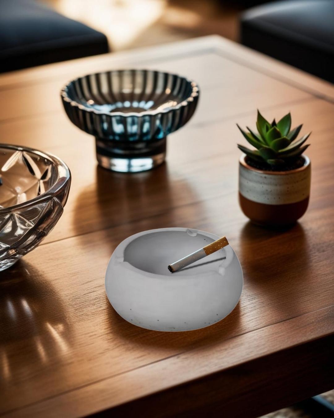 Decorative gray concrete ashtray on a wooden coffee table next to a ceramic bowl in a rustic-modern living room