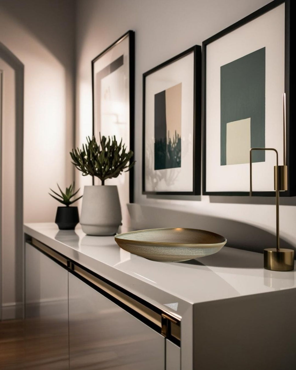 Green and beige reactive glaze porcelain bowl on white entry table in modern hallway with abstract wall art and decorative plants