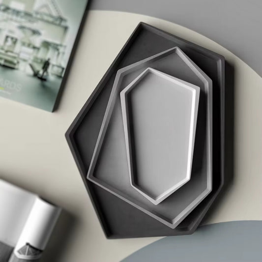 Set of nested hexagonal minimalist trays in various shades of grey, arranged on a modern tabletop.