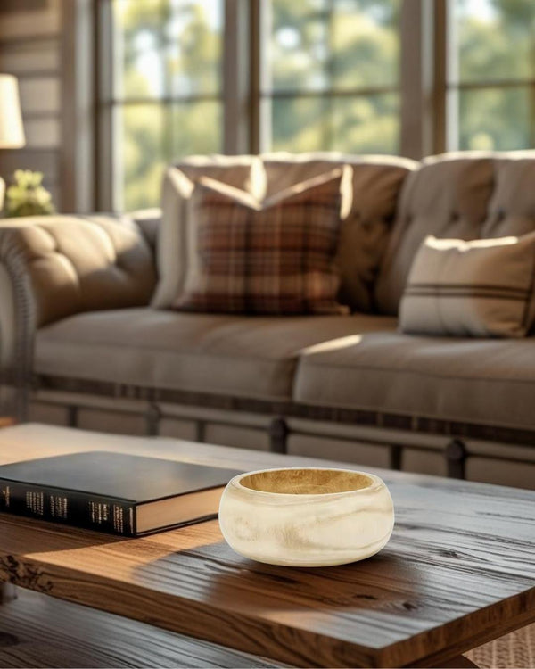 Light wood decorative bowl on a rustic coffee table in a cozy farmhouse style living room with tufted sofa and large windows