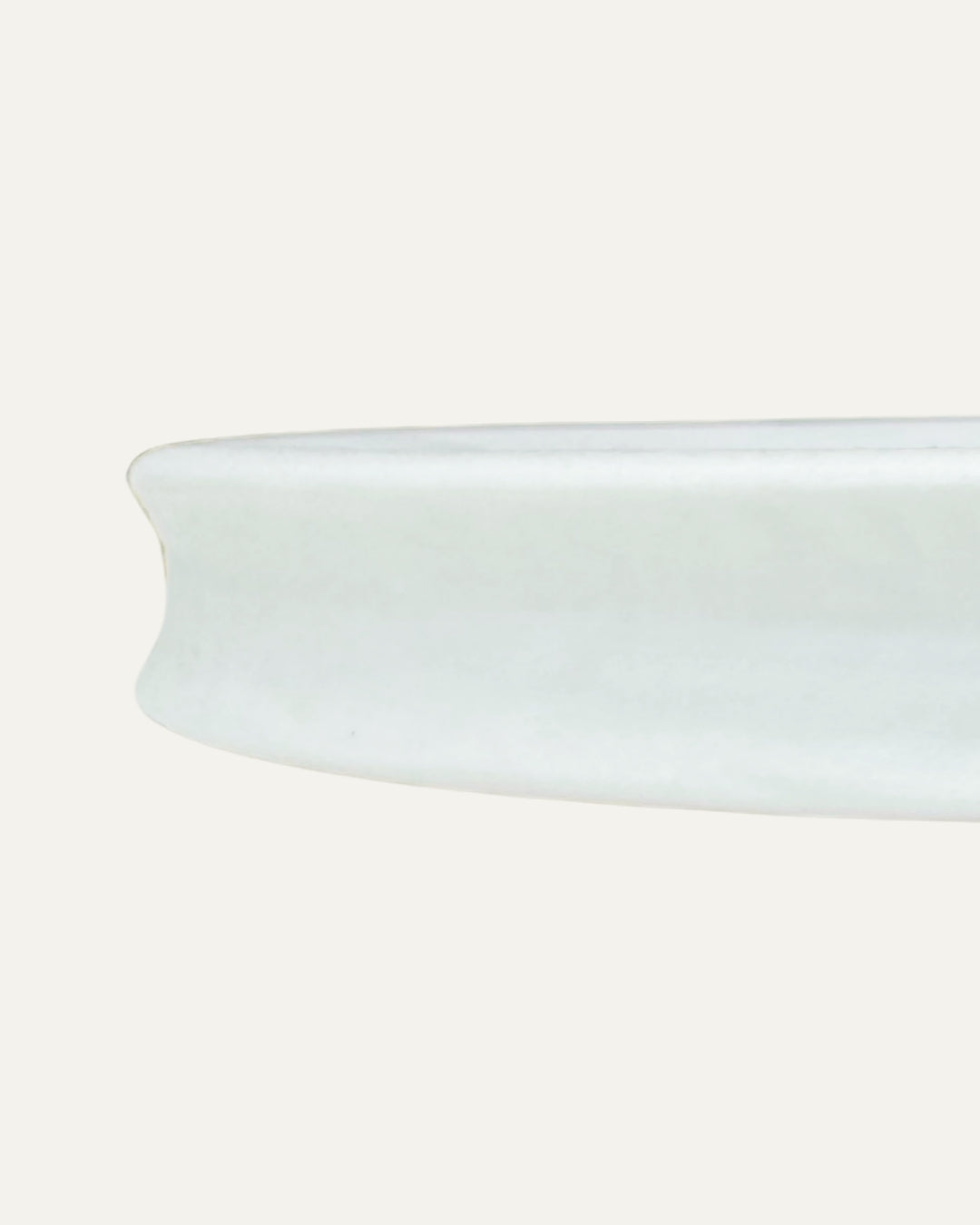 Detalle lateral del borde curvo del plato blanco para postres Luxemburgo sobre fondo claro.