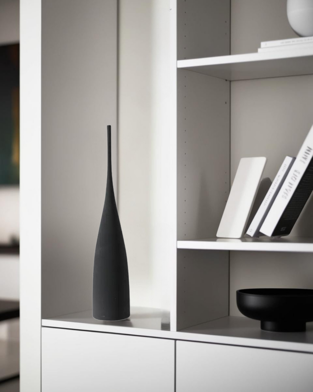 Black long ceramic vase on white modern shelf in minimalist living room decor.