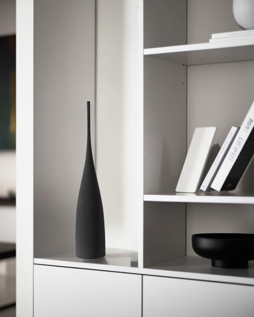 Black long ceramic vase on white modern shelf in minimalist living room decor.