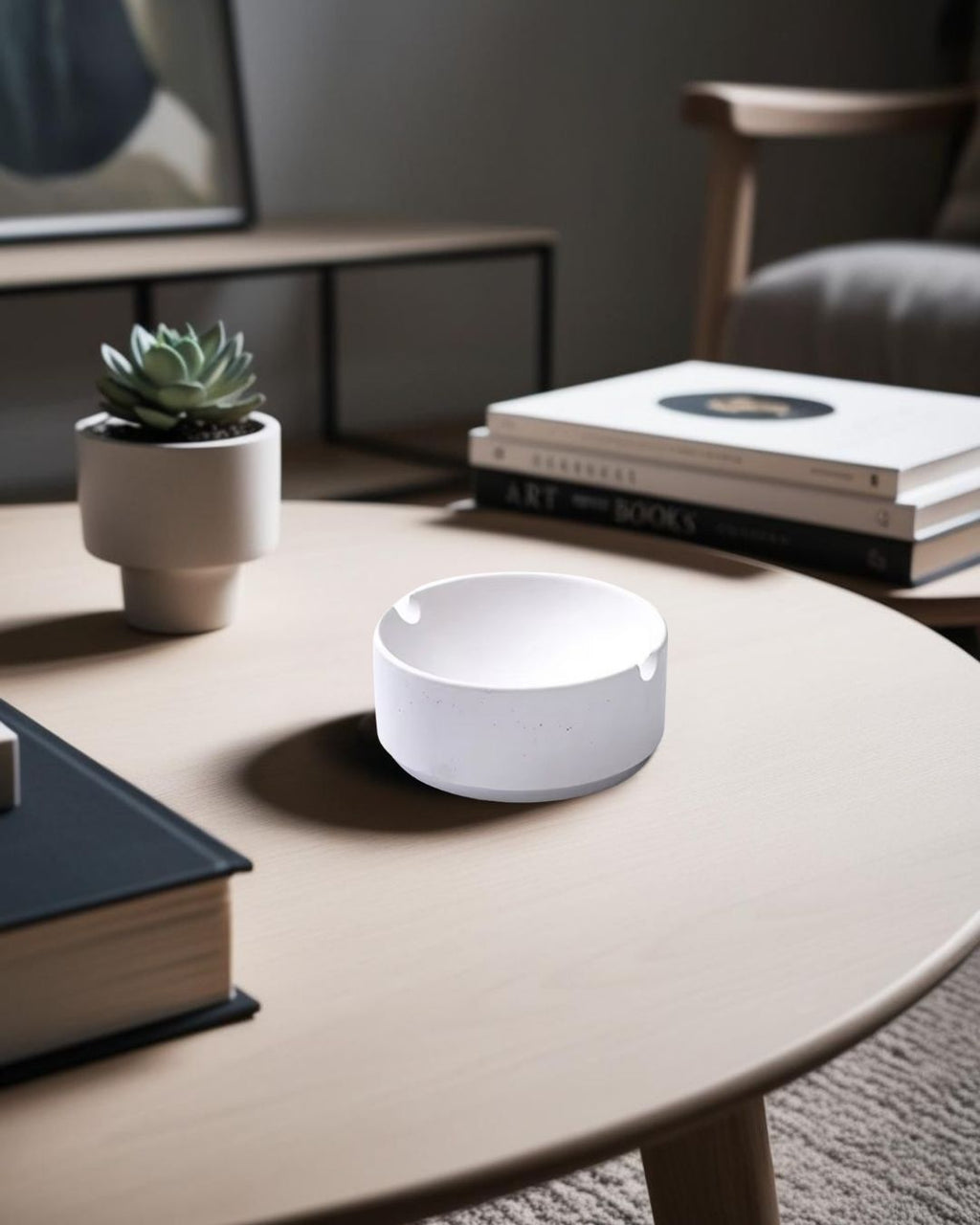 Modern white ashtray on light wooden round table with stacked books and minimal decor