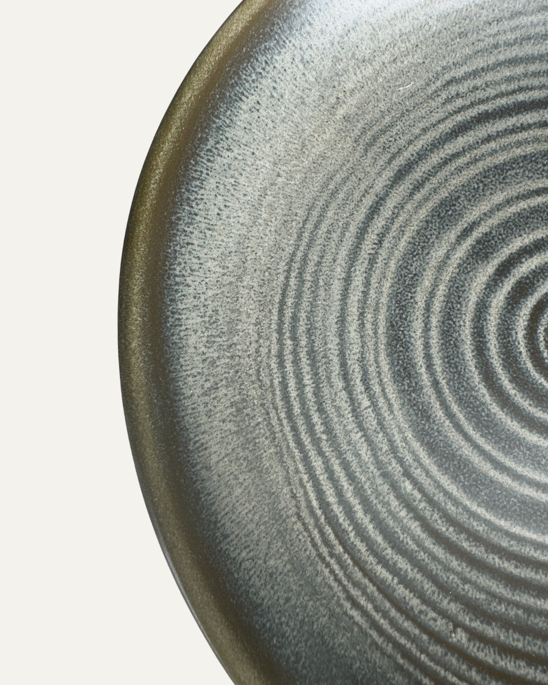 Detalle del plato Brisa gris azulado: anillos concéntricos y borde con matices oliva, vistos de cerca.