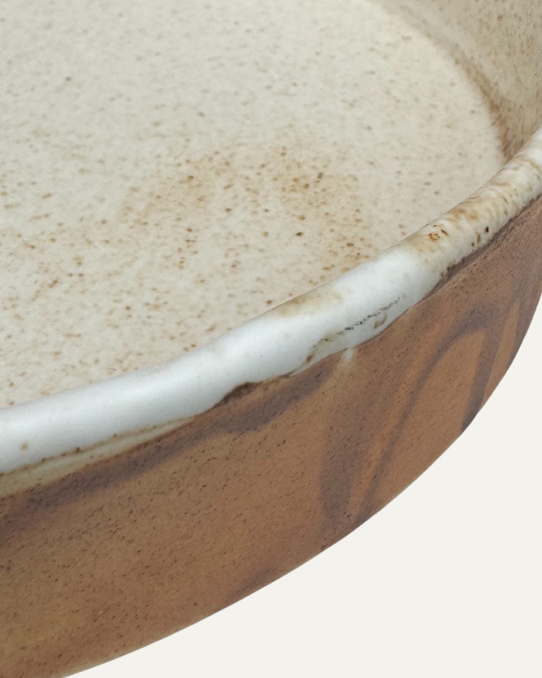 Detalle del borde crema y del interior moteado del plato Rundebrett color miel, con vetas marrones en el exterior.