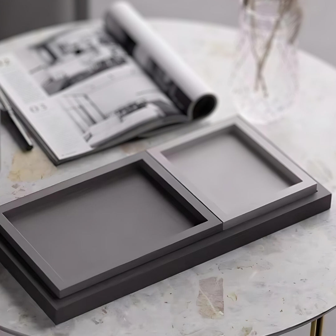 Rectangular nordic minimalist decorative trays in shades of grey, displayed on a marble surface with an open magazine.