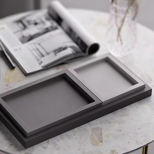 Rectangular nordic minimalist decorative trays in shades of grey, displayed on a marble surface with an open magazine.
