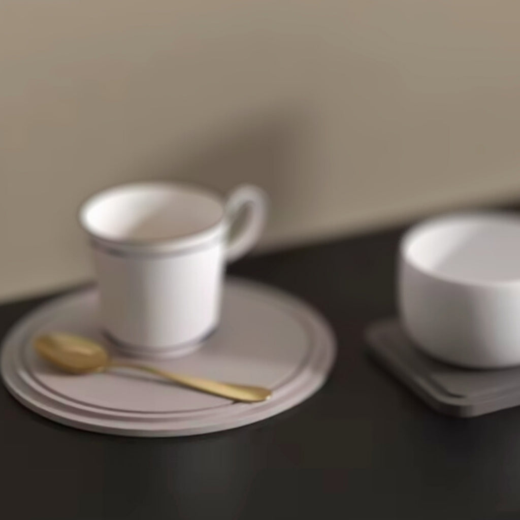 Round and square cup nordic holder trays with white cups and a gold spoon, set on a dark surface.