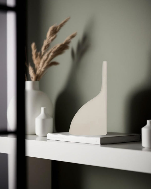 Sculptural white ceramic vase with minimalist design placed on stacked books, styled on a modern Japandi shelf with neutral decor elements.