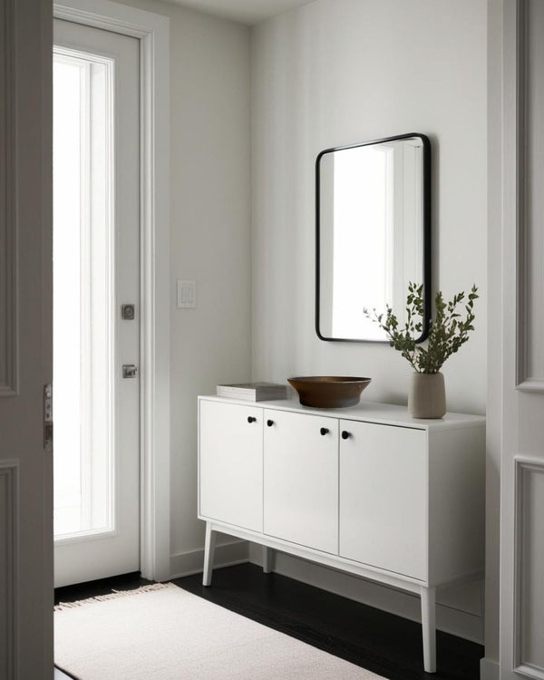 Shallow black decorative porcelain bowl on a white entry table in a bright Scandinavian style entryway with mirror and ceramic vase