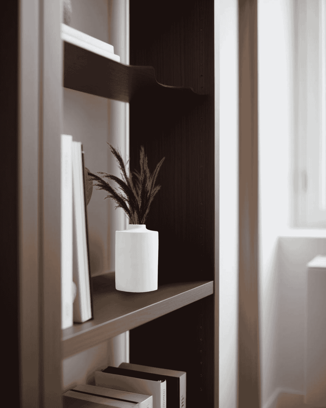 Small concrete vase on a dark bookcase near a window in a minimalist home office

