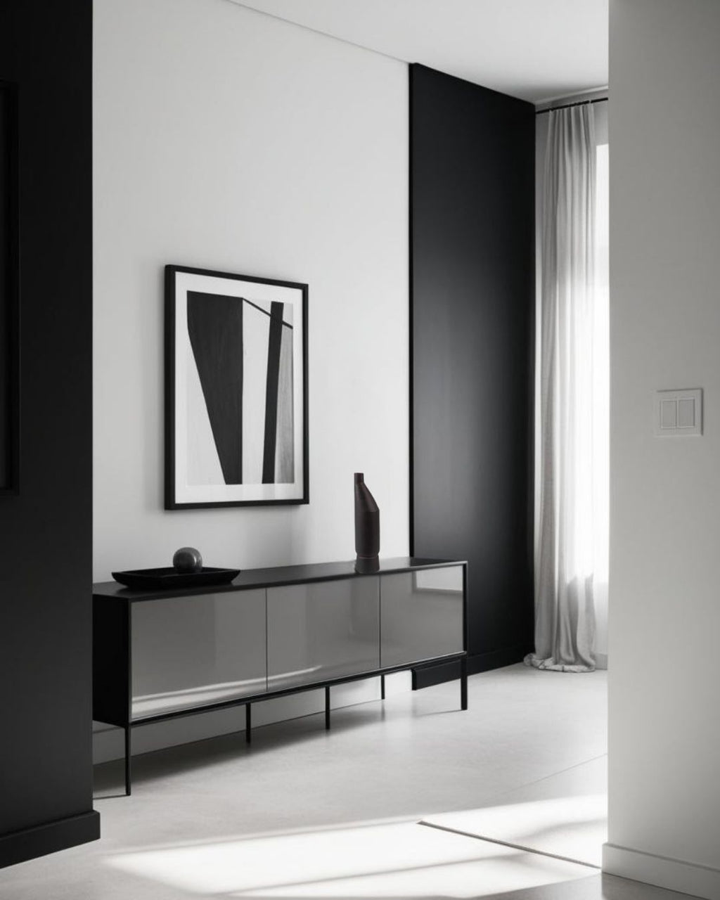 Tall black ceramic vase on a modern black sideboard in a minimalist living room with monochrome artwork and neutral color palette.







