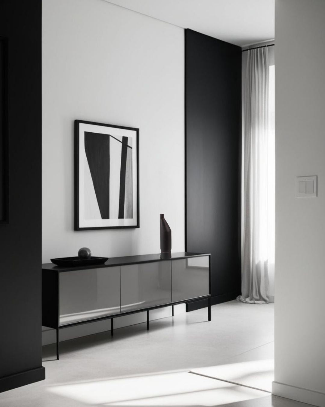 Tall black ceramic vase on a modern black sideboard in a minimalist living room with monochrome artwork and neutral color palette.







